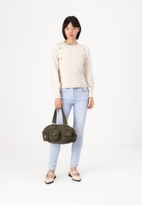 Cream sweater with button details on shoulders, light blue jeans, olive green handbag with pockets, and beige flat shoes.