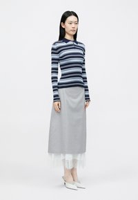 Μπλε ναυτικό και γαλάζιο ριγέ πόλο με μακριά μανίκια και γιακά, σε συνδυασμό με γκρι μακριά φούστα με λευκή δαντέλα στο κάτω μέρος και λευκά ψηλοτάκουνα παπούτσια.