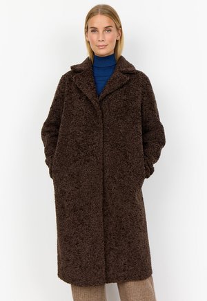 Brun texturerad kappa med en lös passform, notchad krage och fickor. Buren över en blå polotröja. Enkel, odekorerad design.
