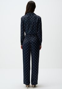 Marineblauwe jumpsuit met lange mouwen, voorzien van een subtiel patroon van kleine witte kruisen, gladde stof en een wijde broekspijpontwerp.