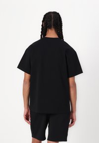 Black short-sleeve t-shirt made of a smooth fabric, featuring a crew neck and a relaxed fit. The back is plain, with no visible logos or patterns.