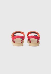 Red and orange sandals with adjustable straps, textured beige sole, and colorful accents. Back view shows dual strap design and soft material.