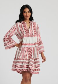 Röd och vit mönstrad klänning med V-ringning, utsvängda ärmar och lagerdesign, med geometriska former och texturerad tyg.