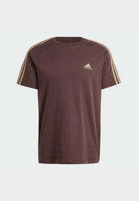 Hnědé bavlněné tričko s krátkým rukávem, třemi zlatými pruhy na každém rameni a malým zlatým logem Adidas na hrudi.