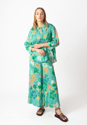 Bloemrijke twee-delige outfit met een losse pasvorm, groene achtergrond, met kleurrijke bloemen in oranje, roze en geel. Zacht materiaal, wijde broekspijpen.
