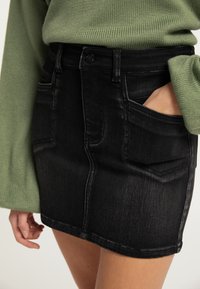 Sort denim nederdel med en tætsiddende design, forlommer og subtile falmninger. Sæt sammen med en struktureret grøn sweater.