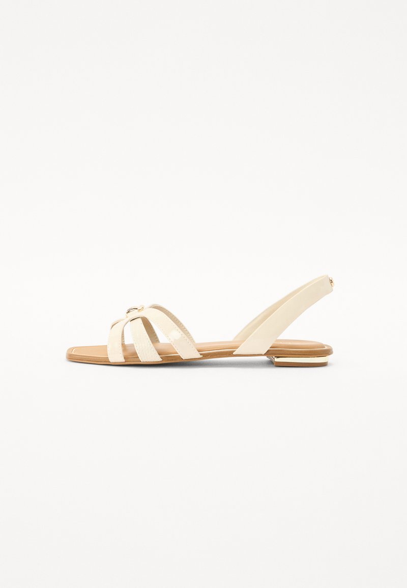 Sandales plates beige avec des brides entrecroisées, un bout pointu et une fine sangle à la cheville. Fini brillant avec un accent doré.