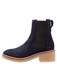 Námornické semišové kotníkové boty s elastickými bočními panely, texturovanou gumovou podrážkou a kontrastním červeným a bílým pruhem po okraji podrážky.