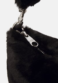 Zwarte nepbonttas met een glanzende zilveren ritsluiting, voorzien van een gedetailleerd UGG-logo en een metalen clipbevestiging.