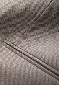 Gros plan sur un tissu gris avec un tissage finement texturé et un détail de couture ajustée formant un bord net.