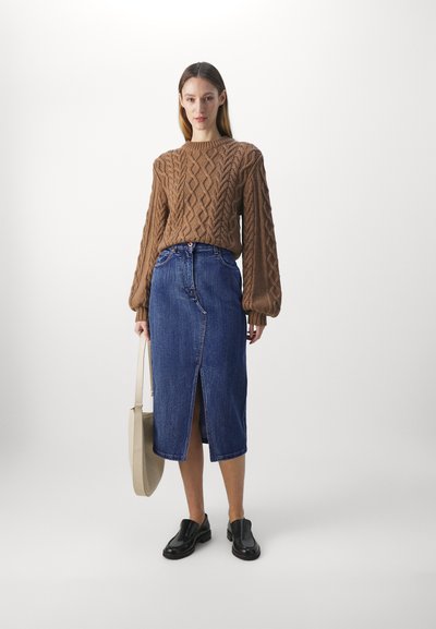 Brun kabelstrikket genser, blå denim blyantskjørt med frontslitt, svarte slip-on sko og beige tote bag. Enkelt og moderne design.