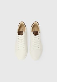 Fehér bőr tornacipők barna nyelvlappal, amelyeken "GANT" logó látható, fehér fűzőkkel és párnázott bézs belső résszel, felülről ábrázolva.