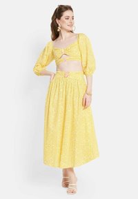 Set a due pezzi giallo a fantasia, composto da un top corto con maniche a sbuffo e una gonna lunga, entrambi con un design testurizzato e dettagli in rosa.