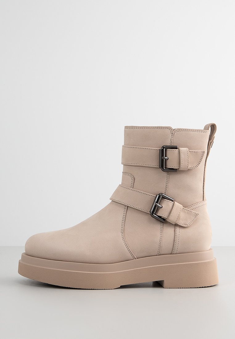 Beige Wildleder-Stiefeletten mit zwei schwarzen Schnallen, einer dicken Plattformsohle und einem eleganten Design. Mit einer Schlaufe auf der Rückseite für ein einfaches Anziehen.