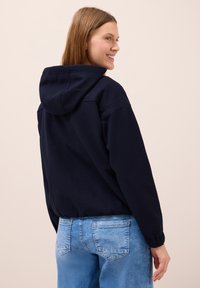 Mörkblå huvtröja med dragsko i huvan, med en avslappnad passform och ribbade muddar, tillsammans med ljusblå denimjeans.