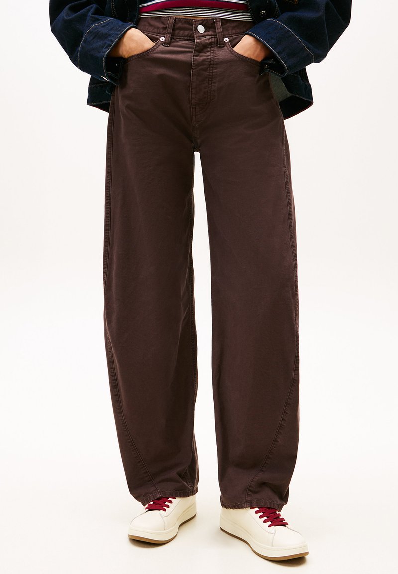 Pantalones de algodón marrones de pierna ancha con cintura alta, bolsillos frontales y cierre de botón, combinados con zapatos blancos y cordones rojos.