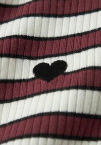 Dzianina w paski w kolorach bordowym, białym i czarnym. W centrum znajduje się mały czarny wzór serca. Całość ma prążkowaną fakturę.