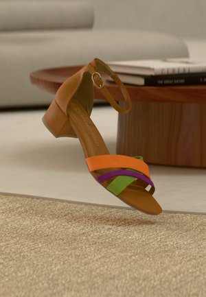 Sandale marron pour femme avec un petit talon bloc et une bride à la cheville, présentant des lanières avant orange, verte et violette, exposée sur un tapis beige.