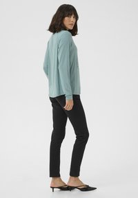 Lichtblauw langemouwen shirt, relaxte pasvorm, met een afgeronde zoom, gecombineerd met smalle zwarte jeans en zwarte hakken. Eenvoudig design en zachte textuur.