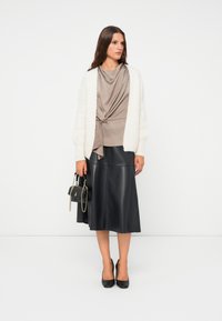 Sweter w kolorze kremowym, luźna bluzka w odcieniu taupe z detalem w postaci węzła, czarna skórzana spódnica midi, czarne obcasy oraz mała czarna torebka z łańcuchem.