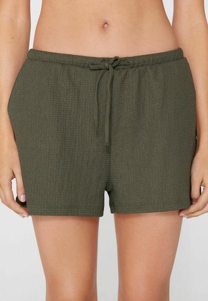 Frau trägt dunkelgrüne Shorts aus strukturiertem Stoff mit elastischem Bund und vorne gebundenem Kordelzug.