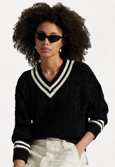 Pull en maille noir avec un col en V, doté de rayures crème sur le col et les poignets. Design cropped avec un tissu texturé.