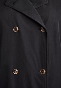 Cappotto nero doppiopetto con rever a scatto, bottoni marroni e una texture di tessuto liscia.