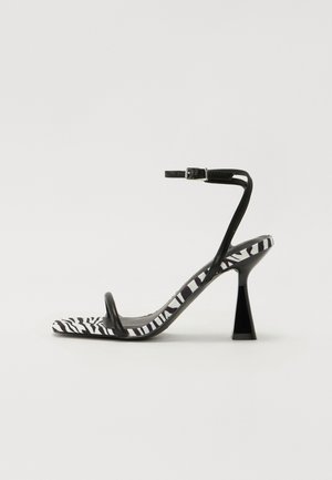 Black and white zebra print high heel sandal with an open toe, slender ankle strap, and a geometric block heel. Smooth texture.