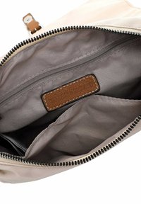 Beige Stoffbeutel mit schwarzem Reißverschluss, grauem Innenfutter, mehreren Fächern und einem braunen Lederetikett, das innen angenäht ist.