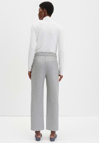 Grijze wijde broek met een gladde textuur, elastische tailleband en een enkele achterzak, gecombineerd met een aansluitend wit longsleeve shirt.