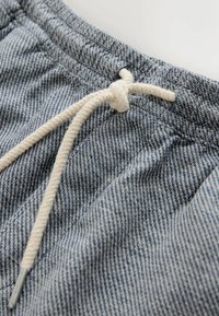 Nahaufnahme von grauen Hosen aus strukturiertem Stoff mit einem weißen Kordelzug, der an einem elastischen Bund zu einem Knoten gebunden ist.