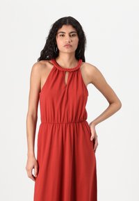 Vestuário vermelho com alças halter, decote trançado, detalhe de buraco e cintura elástica. Tecido suave e design fluido. Sem padrões ou acentos adicionais.