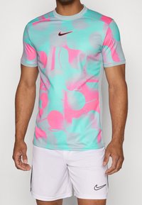 Nike kortärmad träningsskjorta med en ljusblå bas och abstrakta mönster i rosa och grått. Tillverkad av ett slätt, elastiskt material för komfort.