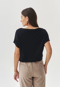 Marineblauw T-shirt met korte mouwen, een relaxte pasvorm, ronde halslijn en een gladde textuur, gecombineerd met lichtbeige high-waisted broek met achterzakken.