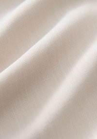 Hellbeiges Gewebe mit glatter Textur und subtilem Webmuster, das sanfte Falten aufweist, die Flexibilität und Flüssigkeit anzeigen.