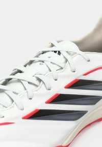 Λευκό αθλητικό παπούτσι με γκρι, κόκκινες και μαύρες λεπτομέρειες. Απαλό δερμάτινο επάνω μέρος με υφασμένα επικάλυψης και παραδοσιακό κλείσιμο με κορδόνια.