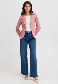 Roze op maat gemaakte blazer met notch revers, gedragen over een witte top, gecombineerd met wijde blauwe jeans en lichtgekleurde hakken. Glad textuur.