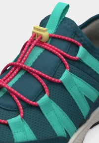 Mørk teal treningssko med turkise stropper og rosa elastiske bungee-snorer festet med en gul knapp på pustende stoffoverdel.