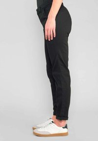 Zwarte slim fit broeken, gemaakt van duurzaam materiaal. Voorzien van riemlussen, zijzakken en omgeslagen zoom, gecombineerd met witte sneakers.