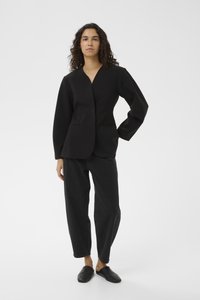 Svart strukturerad kavaj med V-ringning, två framfickor och långa ärmar, tillsammans med lösa svarta jeans och svarta slip-on skor.