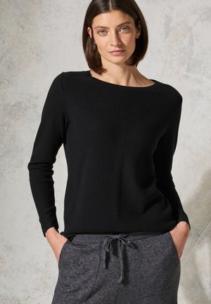 Schwarzer ribbeliger Pullover mit weitem Ausschnitt und langen Ärmeln, kombiniert mit dunkelgrauen Jogginghosen mit Kordelzug, die über eine weiche Textur verfügen.