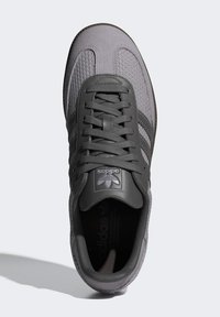 Grå sneaker med en texturerad stickad övre, läderdetaljer och tre ränder. Har en rund tå, vadderad krage och platta snören.