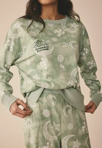 Roheline sidruniga loungewear'i komplekt, millel on valged kuu, tähtede ja laternate mustrid. Kampsunil on ümar kaelus; pükstel on elastne vöökoht ja küljetaskud.