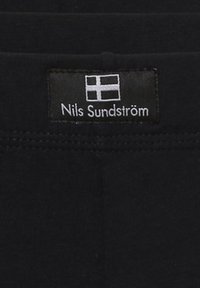 Schwarzer Stoff mit einer glatten Textur, der mit einem Etikett mit dem Namen "Nils Sundström" und einer finnischen Flagge versehen ist.