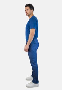 Camiseta de algodón azul combinada con jeans azules, con corte recto, diseño sin costuras y zapatillas blancas. Textura lisa en toda la prenda.