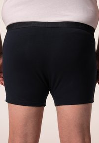Donkerblauwe katoenen boxers hebben een zachte tailleband met een subtiele logo. De stof is glad en sluit nauw aan op de huid.