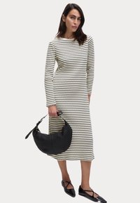 Robe midi à rayures blanches et noires avec manches longues, associée à un sac à main texturé noir et des ballerines noires pointues.