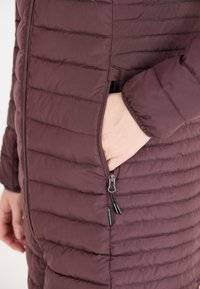 Polstret bordeaux farvet jakke med horisontalt quiltet design, lynlåslommer og lynlås trækstropper; glat tekstur og tætsiddende silhuet.