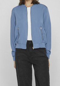 Light blue bomber jacket with a zip front, two side zip pockets, ribbed cuffs, and hem. Smooth fabric with a relaxed fit.