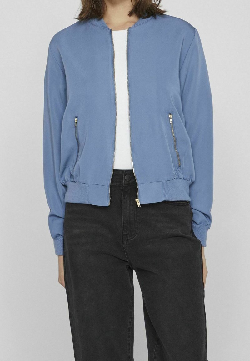 Light blue bomber jacket with a zip front, two side zip pockets, ribbed cuffs, and hem. Smooth fabric with a relaxed fit.